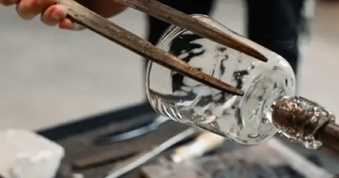 Shaping a glass cup with hand tools.