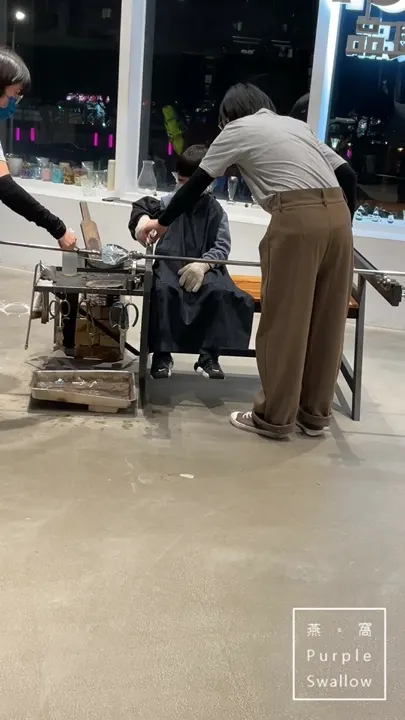 An instructor helping a child shape the glass at the furnace station in the evening.